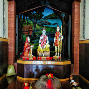 A temple shrine displaying colorful statues of Mata Shabari kneeling before a seated Lord Rama and a standing Lakshmana, set against a painted forest backdrop.